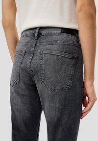 Jean en denim gris avec une taille medium, comportant deux poches arrière et une texture légèrement délavée. Étiquette de ceinture ajustable visible.