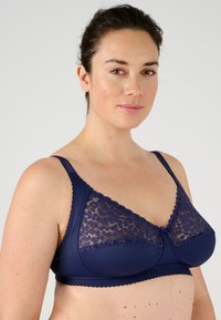 Sujeta de azul marino con paneles de encaje, bordes con forma de ondas y tirantes ajustables. Tejido suave con una textura lisa y patrones florales sutiles.