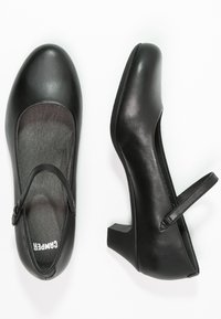 Chaussures Mary Jane en cuir noir avec bout arrondi, petit talon carré et bride réglable. Texture lisse et design minimaliste.