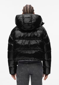 Crna, skraćena puffa jakna s sjajnom završnom obradom, oversized kapuljačom i quilted dizajnom. Ima elastične manžete i opušteni kroj.