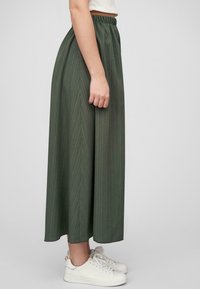 Grønn, plissert maxiskjørt med elastisk midje, med et vertikalt stripemønster. Brukt med hvite joggesko.