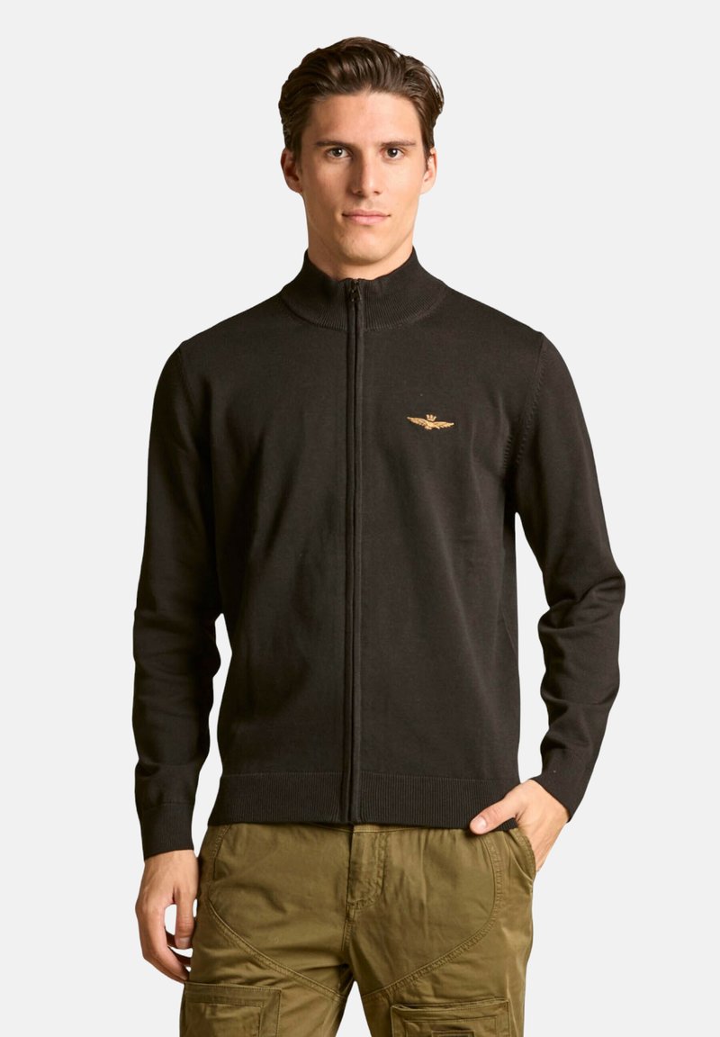 Maglione nero con zip frontale e collo alto, con logo dorato sul petto. Realizzato in tessuto knit liscio con polsini e orlo a costine.