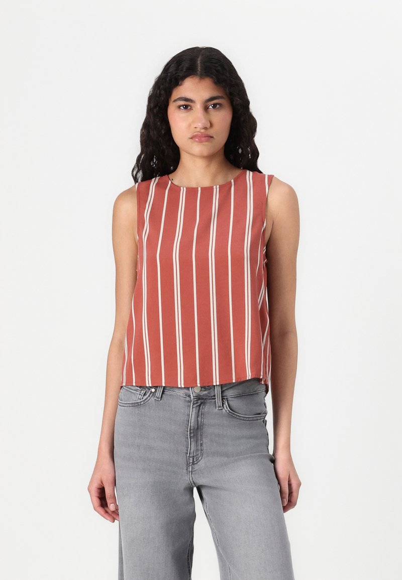 Rød ærmeløs crop top med lodrette hvide striber, rund halsudskæring og løs pasform. Sammen med højtaljede grå jeans.