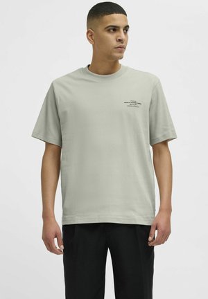 Lichtgrijs T-shirt met korte mouwen en ronde hals, met zwarte tekst aan de bovenste linkerkant. Gemaakt van katoen, met een soepele textuur.