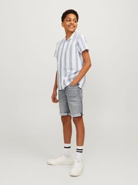 Chemise à manches courtes, rayée bleu clair et blanche, shorts en denim, baskets blanches, accompagnée de chaussettes rayées noir et blanc.