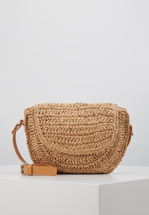 Mała pleciona słomkowa torebka na ramię z zaokrągloną klapką i odpinanym paskiem ze skóry w kolorze naturalnym, umieszczona na białej powierzchni na jednolitym tle.