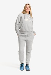 Grå hoodie och set med byxor, med en framficka, elastiska ärmar och en logga på bröstet. I kombination med blå sportskor.