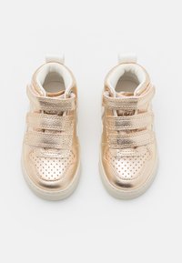 Metalliseeritud kuldsed kõrgete tõusudega sneakerid kolme Velcro rihmaga, perforeeritud detailide, valgete aksessuaaride ja mugavust pakkuva pehmendusega.