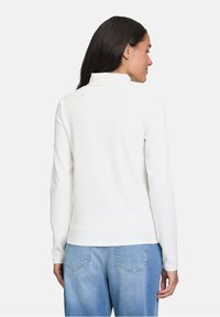 Weißer, gerippter Rollkragenpullover mit langen Ärmeln. Er zeichnet sich durch eine taillierte Silhouette aus und hat eine glatte Textur, kombiniert mit hellblauen Jeans.