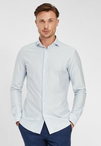 Camicia a maniche lunghe a righe blu chiaro e bianche con colletto abbottonato, orlo curvo e texture in cotone morbido. Abbinata a pantaloni blu navy.