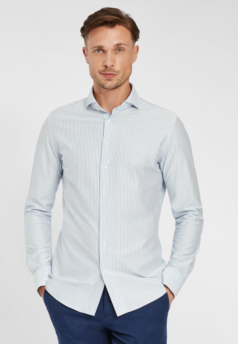 Camicia a maniche lunghe a righe blu chiaro e bianche con colletto abbottonato, orlo curvo e texture in cotone morbido. Abbinata a pantaloni blu navy.