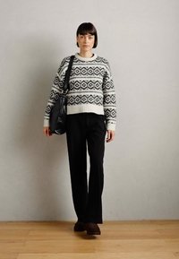 Crochet-style sweater in white and black with geometric patterns, paired with black wide-leg pants and dark brown slip-on shoes.