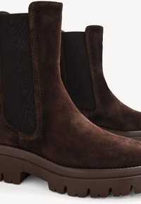Paire de bottines en daim brun foncé avec panneaux latéraux élastiques et semelles épaisses à crampons, sur un fond clair uni.
