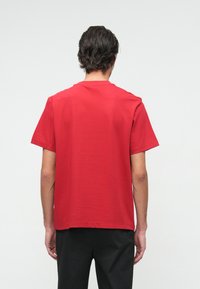 Czerwona koszulka z krótkim rękawem z bawełny, z klasycznym okrągłym dekoltem i luźnym krojem, o gładkiej fakturze i prostym wzorze.