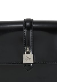 Borsa in pelle verniciata nera con finitura lucida, dotata di chiusura a lucchetto in argento, bordi cuciti e una superficie morbida. Accentuata da un dettaglio con il logo.