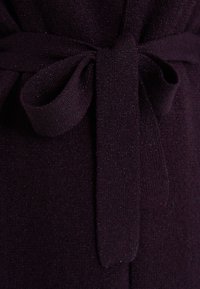 Tissu tricoté violet foncé noué en un nœud de ruban texturé, mettant en valeur la douceur, la chaleur et le confort du matériau.