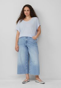 Maglietta azzurra chiara oversize con scollo a V abbinata a jeans in denim sbiadito a gamba larga. Le scarpe flat argento completano l'outfit con un tocco di texture.