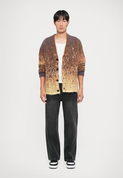 Kootud kardigan pruunide ja kollaste gradientvärvidega, millel on suured mustad nööbid, tekstureeritud kangas ja mugav lõige. Kombineeritud tumedate teksadega.