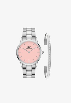 Hõbedane metallkell ümmarguse korpuse ja roosa kellapinnaga, millel on hõbedased tundmärgid. Lisatud on eraldi graveeritud käevõru, millel on "Daniel Wellington."