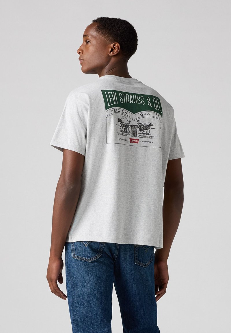 Gray cotton T-shirt featuring a large green and black graphic print on the back, with "LEVI STRAUSS & CO" and two figures. Blue jeans visible.