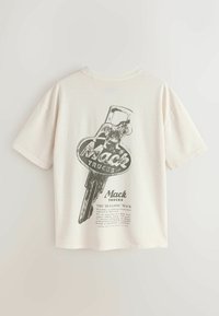 Chemise à manches courtes écrue avec un graphisme clé Mack Trucks vintage noir et du texte au dos.