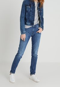 Blue denim jacket with a cropped design, paired with light grey T-shirt and tapered blue jeans. White sneakers complete the outfit.