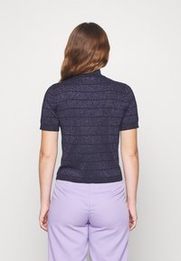 Lyhythihainen, vartalonmyötäinen paita tummansinisenä, jossa metallilankaiset yksityiskohdat. Mallissa on vaakaraitoja ja korkea kaulus; sileä pinta.