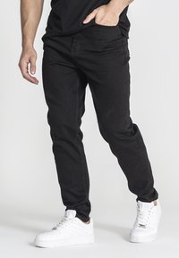 Pantalones de mezclilla negros con corte ajustado, con una textura suave, diseño minimalista y combinados con zapatillas blancas.