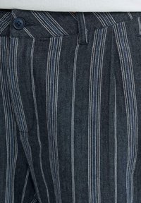 Pantalon bleu marine à fines rayures verticales blanches et bleu clair, doté d'une fermeture à boutons et de passants pour ceinture à la taille.