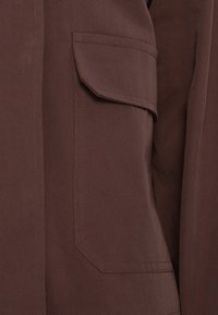 Καφέ βαμβακερό σακάκι με τσέπη τύπου patch, ορθογώνιο καπάκι, κάθετη ραφή και υφή με ανάγλυφο φινίρισμα.