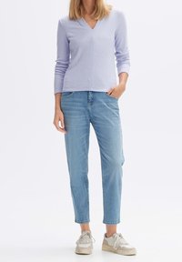 Ljust lila ribbad långärmad topp med V-ringning, i kombination med ljusblå raka jeans och beiga sneakers med vita accenter.