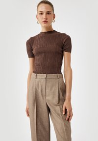 Brun ribstrikket top med korte ærmer, featuring en rund halsudskæring. Kombineret med lysebrune højtaljede plisserede bukser for et skræddersyet look.