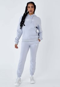 Lichtgrijze hoodie en sweatpants set, gemaakt van zachte stof. Hoodie heeft een voorzak en bedrukt logo. Broek heeft elastische boorden.