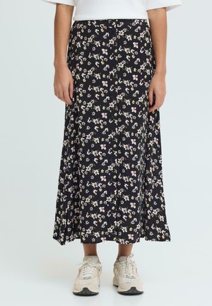 Kobieta ubrana w czarną, kwiatową midi spódnicę zapinaną na guziki z przodu, w połączeniu z białymi trampkami i białą bluzką.