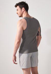 Grå ribbet tanktop parret med stribede shorts; har et tætsiddende design og minimalistisk stil, der viser ryg- og arm-tatoveringer.