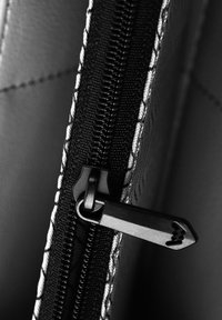 Black zipper with metallic pull tab on textured material, featuring detailed stitching alongside the zip and smooth interior.