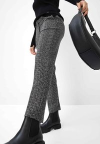 Graue Hahnentrittmuster-Hosen aus strukturiertem Stoff mit schmalem Schnitt. Kombiniert mit schwarzen Knöchelstiefeln und einer schwarzen Schultertasche.