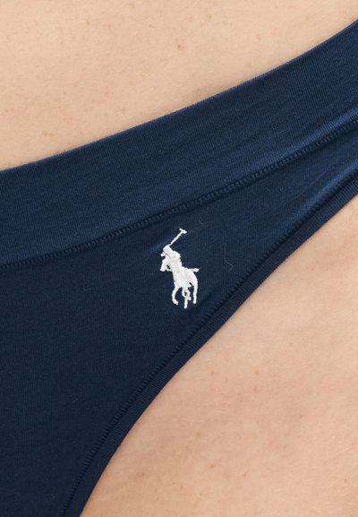 Πλησιάζοντας υφάσμα ναυτικού μπλε με λευκό κεντητό λογότυπο παίκτη πόλο σε φόντο χρώματος δέρματος.