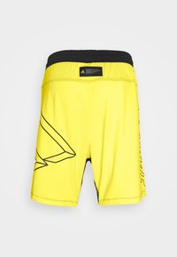 Gule sportsshorts med sorte accenter, der har et geometrisk design og elastisk taljebånd. Glat tekstur med syningsdetaljer.