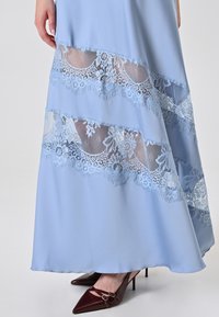 Hellblaue Robe mit transparenten spitzen Einsätzen mit Blumenmustern. Ein glattes, fließendes Material, kombiniert mit kastanienbraunen High Heels.