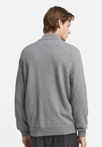 Gråstickad tröja med avslappnad passform, långa ärmar och ribbat nederkant. Texturerad tyg med en slät yta som visar en enkel design.