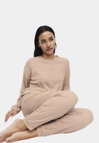 Žebrovaná lehce béžová souprava na domácí nošení, která zahrnuje dlouhý rukáv a kalhoty, oboje z měkkého materiálu s volným střihem.