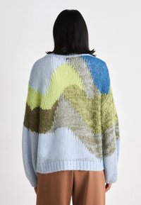 Pull en tricot de couleur bleue douce, avec un motif ondulé de vert, brun et bleu clair. Coupe ample avec un col rond et un ourlet côtelé.