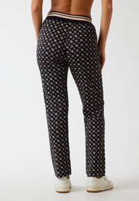 Pantaloni neri con motivo, caratterizzati da un design testurizzato e da una cintura a righe. Presentano una silhouette aderente e gambe affusolate. Sneakers bianche classiche.