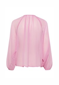 Blouse légère en rose pâle avec de longues manches bouffantes, un col rond et une coupe fluide. Tissu texturé avec des plis subtils.