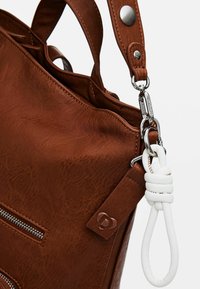 Braune Kunstleder-Handtasche mit silberner Hardware, strukturiertem Oberflächen und oberen Griffen sowie einem weißen geflochtenen Akzent an der Seite. Sichtbare Reißverschlussdetails.