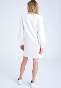 Vit långärmad klänning med puffärmar, rundad halsringning, midj längd och slät tyg. Matchad med vita sneakers.