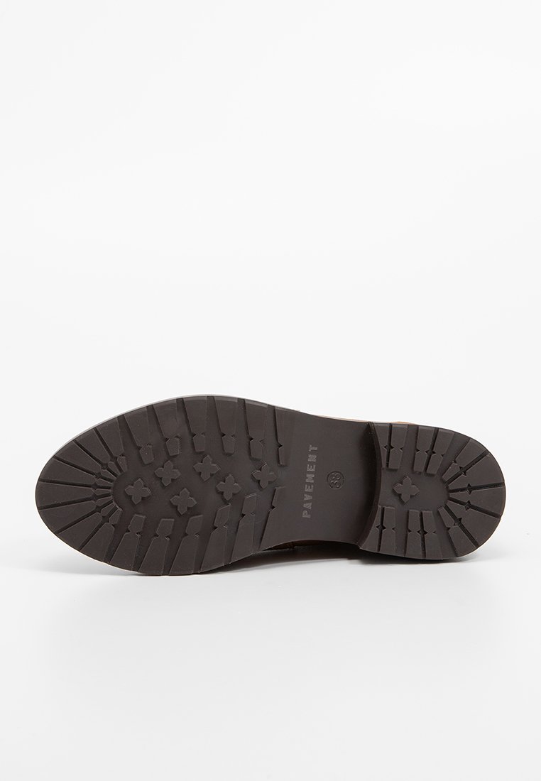 Suela de zapato de goma marrón con una superficie texturizada que presenta surcos y patrones en forma de flor, marcada con "PAVEMENT" y un logo circular.