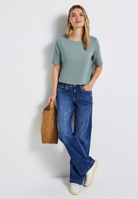 Lichtgroene top met korte mouwen, gecombineerd met wijde blauwe denim jeans en witte sneakers, en een tan suède tas. Eenvoudig ontwerp en relaxte pasvorm.