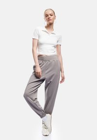 Hvid ribbet kortærmet polo skjorte med tre knapper, parret med lysegrå elastiske joggere og hvide sneakers.